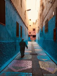 Rear view of woman walking in alley amidst buildings