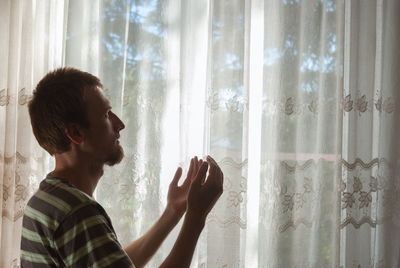 Side view of woman looking through window at home