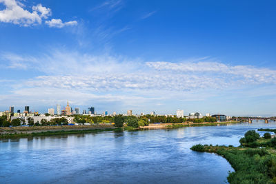 View of buildings by river against blue sky