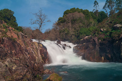 Scenic view of waterfall in forest against sky