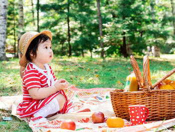 Cute asian infant girl in a stripped red dress and srtaw hat on a picnic in the park