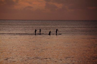 Silhouette people on sea against sky during sunset