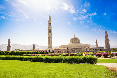 Garden by mosque in city against blue sky