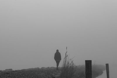 Rear view of man walking on field during foggy weather