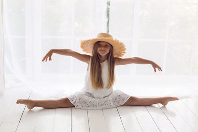 Girl in a white dress in a straw hat sitting on a twine on the white floor in the room