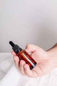 Cropped hand of woman holding bottle against white background