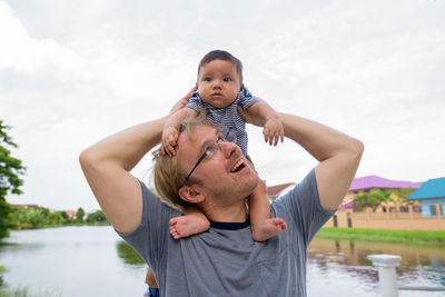 Portrait of father and son holding baby against sky