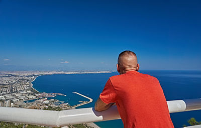 Rear view of man looking at sea against blue sky