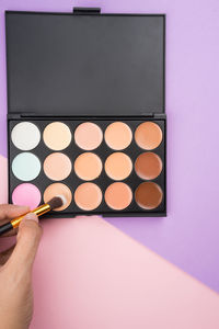 Close-up of hand holding brush over beauty product on two tone background