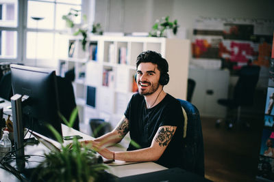 Portrait of smiling young man using computer while sitting at office