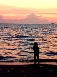 Silhouette of people standing by sea at sunset