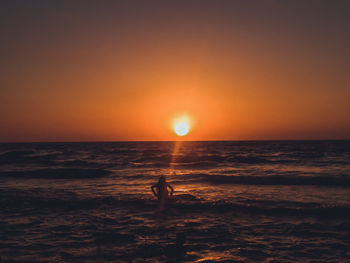 Silhouette woman in sea against sky during sunset