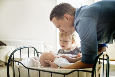 Father putting baby girl in cradle while daughter looking at them