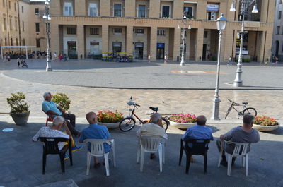 Rear view of people sitting on street against buildings in city