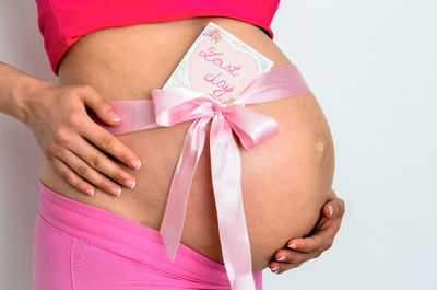 Midsection of woman standing against pink background