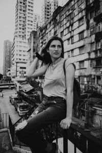 Portrait of young woman sitting against buildings in city