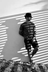 Full length of man wearing hat leaning on wall during sunny day