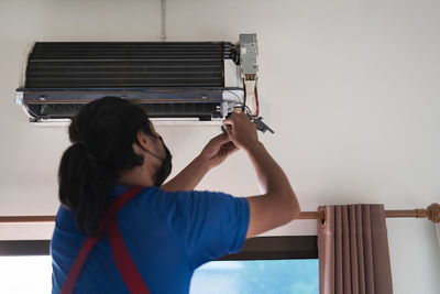 Rear view of man repairing air conditioner