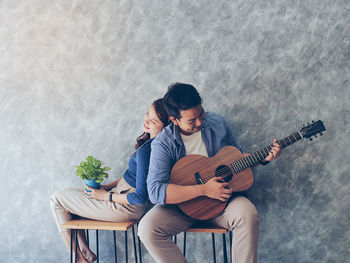 Man playing guitar by woman holding plant