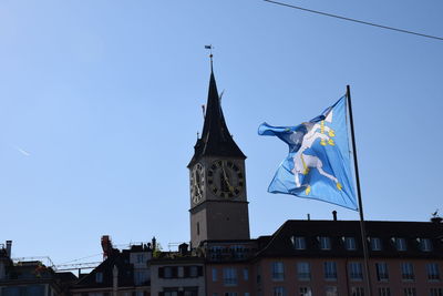 Low angle view of flags against buildings against clear blue sky.