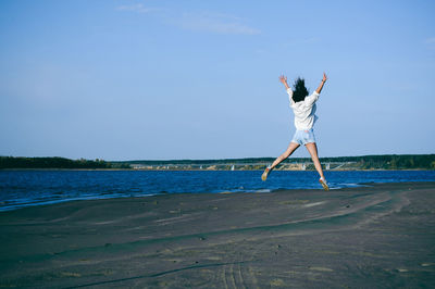 Woman jumping at beach against sky