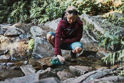 Woman taking pure water to bottle from mountain stream during trekking in mountains