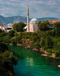 Mosque by green river against sky