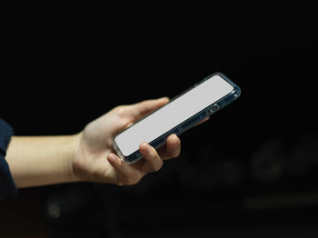 Close-up of hand of woman holding mobile phone against black background