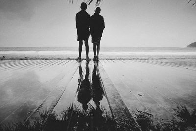 Rear view of couple standing on beach against sky