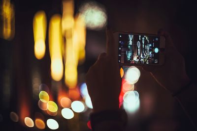 Cropped image of man photographing illuminated city at night