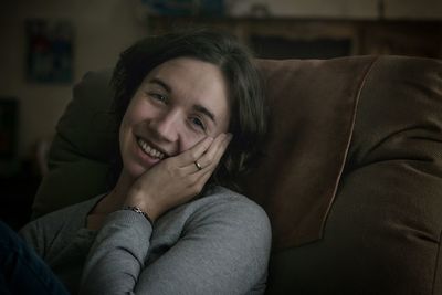 Close-up of smiling mid adult woman leaning on armchair at home