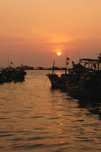 Fishing boats moored on sea against sky during sunset