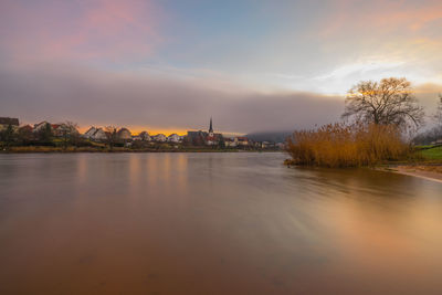 Scenic view of river by buildings against sky during sunset