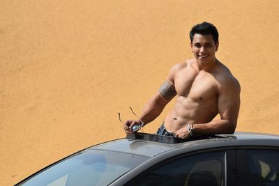 Shirtless smiling muscular man standing in sun roof at desert