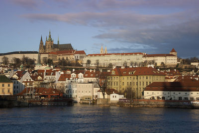 Buildings by river against cloudy sky