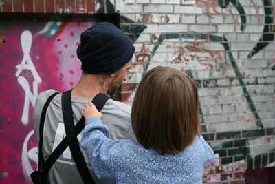 Rear view of daughter with father against graffiti wall