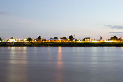 Illuminated buildings by sea against sky