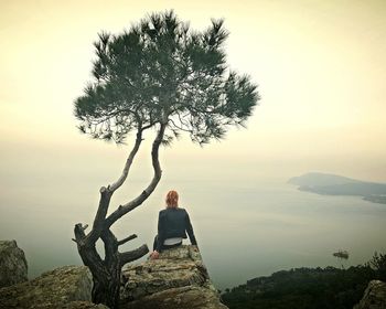 Rear view of woman sitting on rock against sky