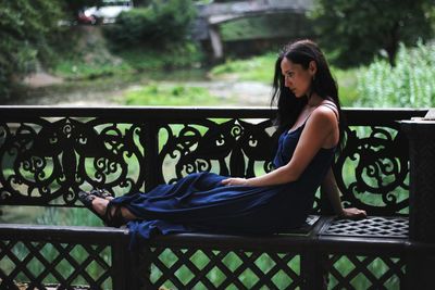 Young woman sitting on railing in park