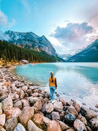 Man standing on rock by lake against sky