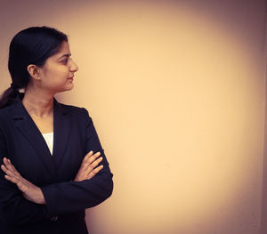 Young woman looking away while standing against wall