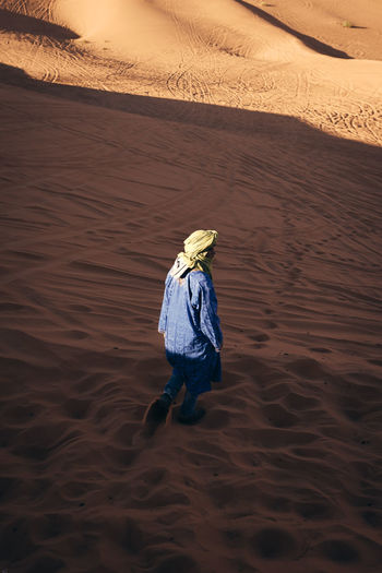 REAR VIEW OF PERSON WALKING ON SAND AT BEACH