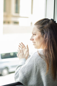 Side view of woman looking through window