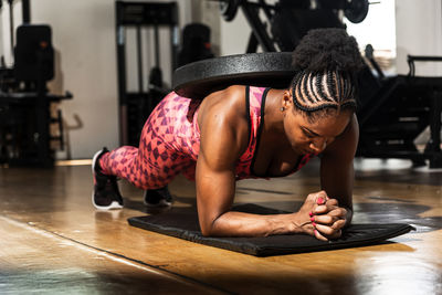 Woman training in modern light studio. doing a plank with weight on your back. flexion on weights.