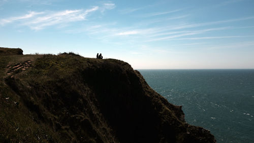 People standing on cliff by sea against sky