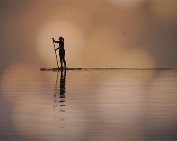 Silhouette man standing in sea against sky during sunset