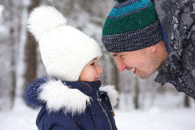 Dad and daughter look at each other closely in warm clothes, hats with a pompom on the 