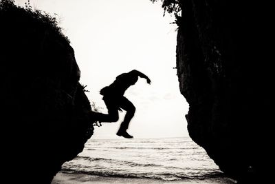 Silhouette man on rock by sea against clear sky