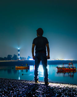 Rear view of man standing against illuminated lighthouse at night