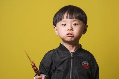 Portrait of boy eating food while standing against yellow background